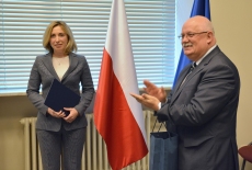 Na tle flag Polski i UE stoją: Iryna Vereshchuk - trzyma teczkę z certyfikatem i Dyrektor KSAP - klaszcze. 