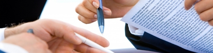 dwie dłonie trzymające długopisy i zadrukowaną tekstem kartkę 